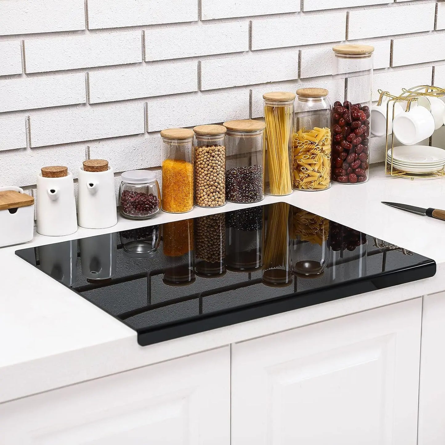 Moderne zwarte acrylic snijplank van DHProducts op een wit keukenblad, omringd door glazen voorraadpotten en keukenaccessoires.