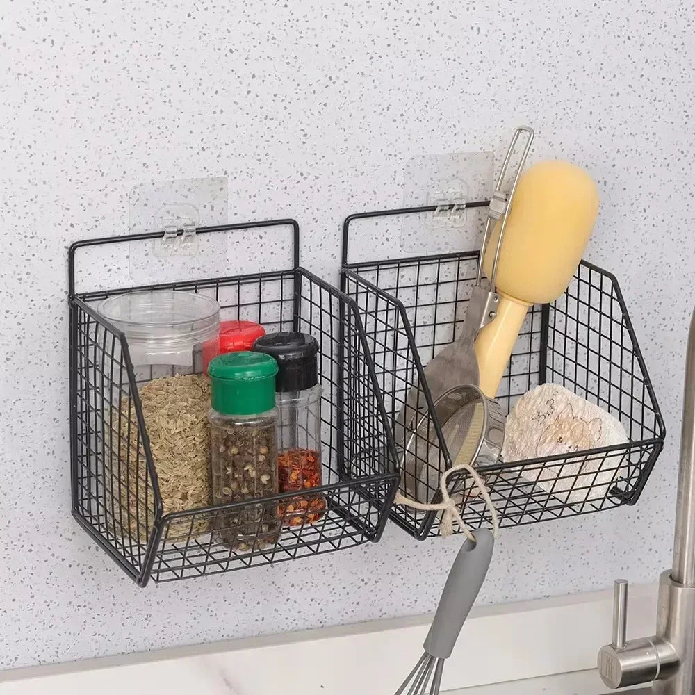 "Zwarte metalen wandmandjes in de keuken, bevestigd met transparante plakhaakjes, gevuld met kruidenpotjes, keukengerei en een schuursponsje.
