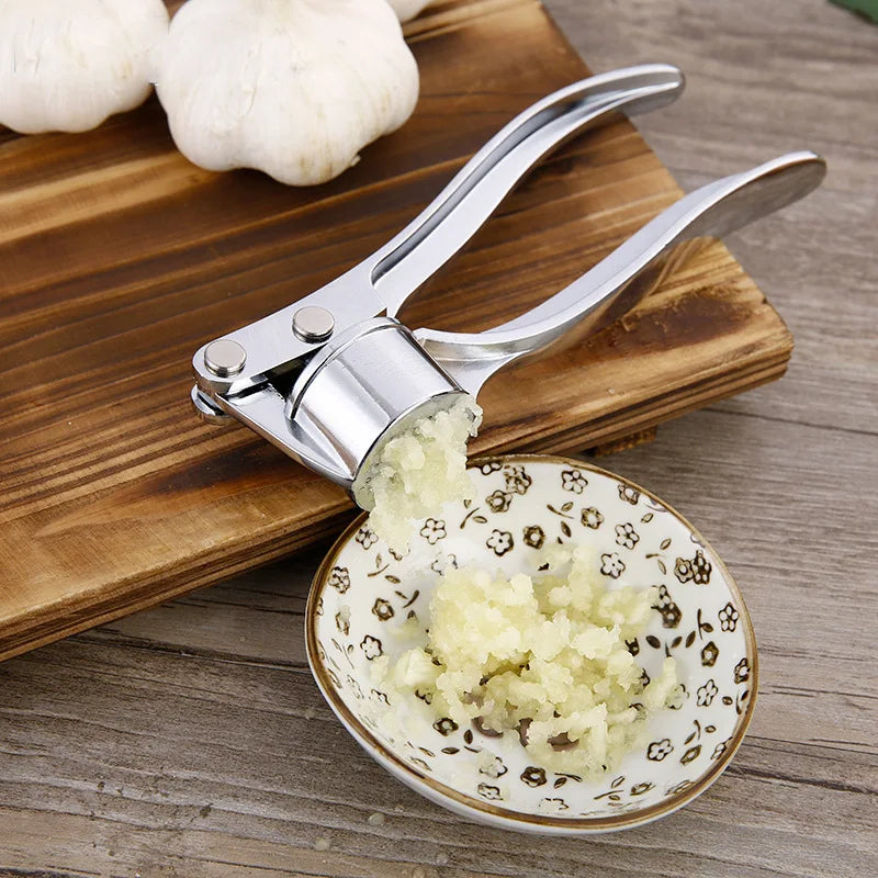 Roestvrijstalen garlic crusher perst verse knoflook boven keramisch schaaltje – snel, schoon en effectief.