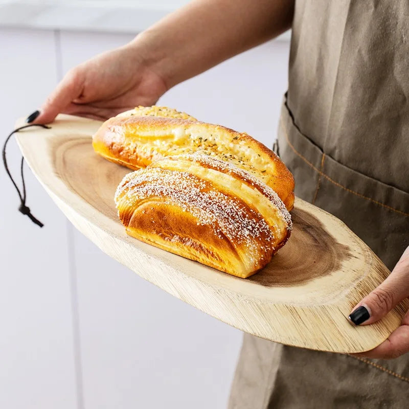 Hand die een ovale acaciahouten serveerplank vasthoudt met vers gebakken broodjes, ideaal als snijplank of presentatieplank voor in de keuken.